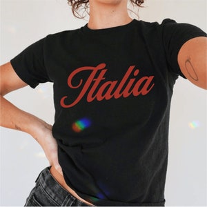 以下が含まれることがあります： 赤い筆記体で「イタリア」と書かれた黒いTシャツです。