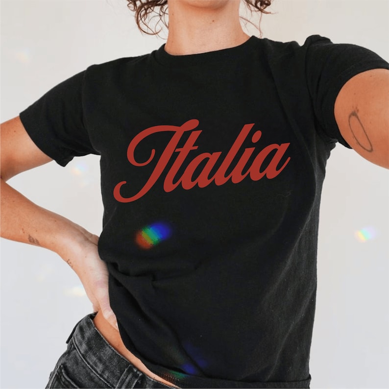 以下が含まれることがあります： 赤い筆記体で「イタリア」と書かれた黒いTシャツです。