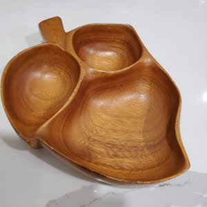 Könnte beinhalten: Eine Servierschale aus Holz mit drei Abschnitten, geformt wie ein Blatt. Die Schale ist aus hellbraunem Holz und hat eine natürliche Oberfläche.