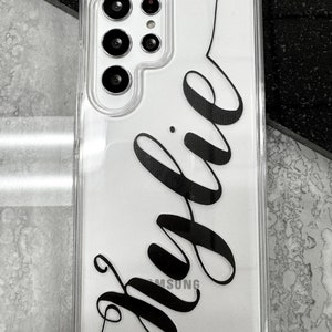 May include: A clear phone case with a black inscription that says "Julie" on a white background. The case has a camera cutout on the back.