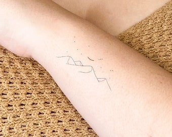 May include: A close-up of a person's arm with a small tattoo of mountains and a crescent moon.