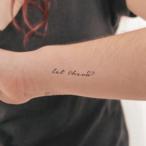 Könnte beinhalten: Ein temporäres Tattoo mit dem Text "let them" gefolgt von einem kleinen Herzen.