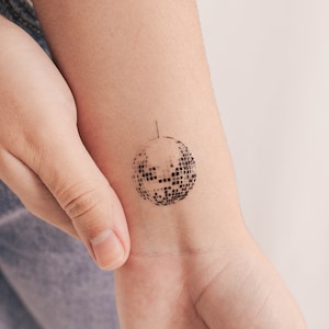 Könnte beinhalten: Ein temporäres Tattoo eines schwarz-weißen Discoballs auf dem Arm einer Person.