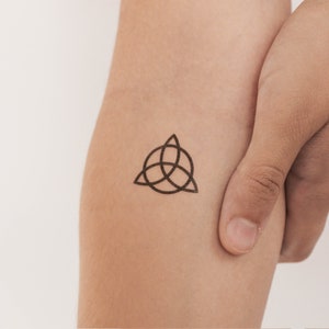 May include: A black and white temporary tattoo of a triquetra symbol, a three-pointed knot, on a person's arm.