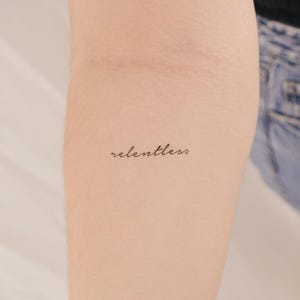 Peut inclure: Gros plan sur le bras d'une personne avec un petit tatouage qui dit "relentless" en écriture cursive.