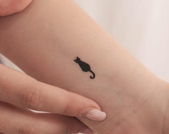 May include: A small black cat silhouette tattoo on a person's wrist.