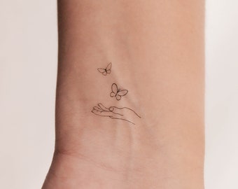 May include: A simple line drawing tattoo design of a hand with two butterflies flying away from it.