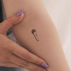 Peut inclure: Un petit tatouage de microphone noir et blanc sur le bras d'une personne.