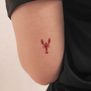 Puede incluir: Un pequeño tatuaje de langosta roja en el brazo de una persona.