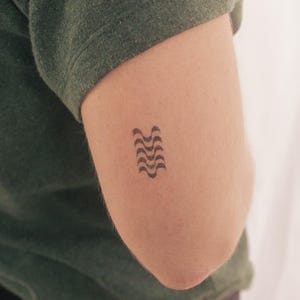 May include: A black and white geometric tattoo design of wavy lines on a person's arm.