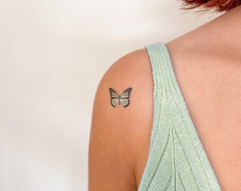 May include: A small, green butterfly temporary tattoo on a person's shoulder.