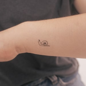 May include: A simple line drawing tattoo of a snail on a person's arm.