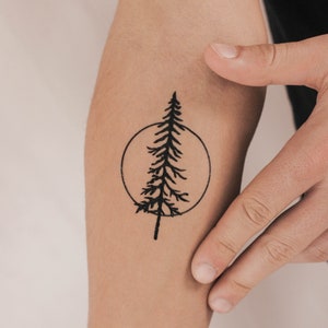 May include: A black temporary tattoo of a pine tree inside a circle on a person's arm.