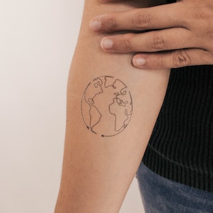 Op de afbeelding: Een eenvoudige lijntekening van de aarde met pijlen die de rotatie aangeven, getatoeëerd op de arm van een persoon.