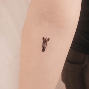 Puede incluir: Un pequeño tatuaje de cabeza de cebra en blanco y negro en el brazo de una persona.