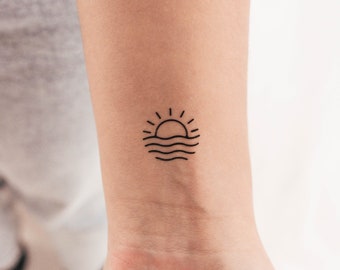 Puede incluir: Un tatuaje simple de línea de un sol poniéndose sobre el océano. El tatuaje es negro y está en la muñeca de una persona.