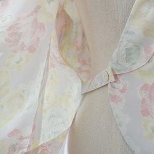 May include: A white blouse with a floral print featuring pink, yellow, and green roses. The blouse has a large, rounded collar with a button closure.