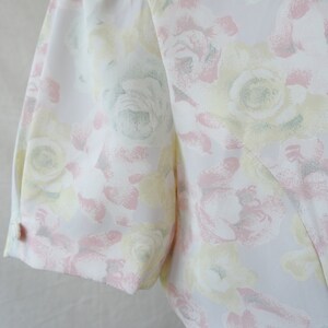 May include: A white dress with a floral pattern in shades of pink, yellow, and green. The dress has a short sleeve and a button on the sleeve.