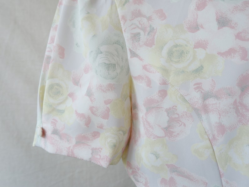 May include: A white dress with a floral pattern in shades of pink, yellow, and green. The dress has a short sleeve and a button on the sleeve.
