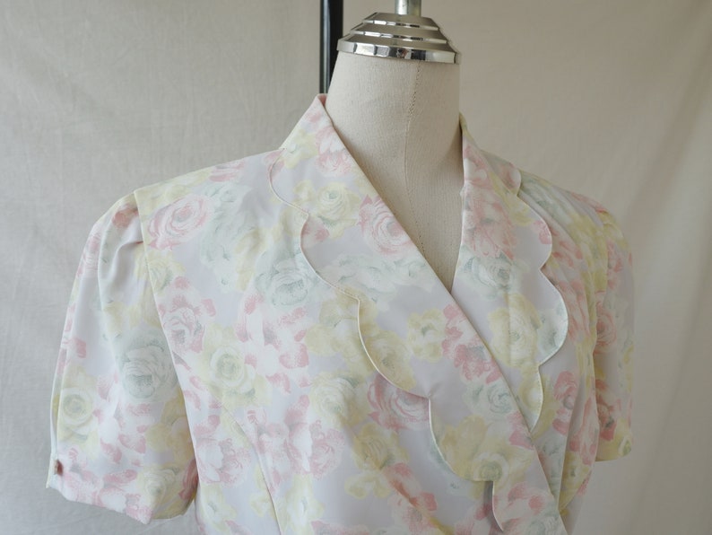 May include: A white blouse with a floral print featuring pink, yellow, and green flowers. The blouse has a scalloped collar and short sleeves.