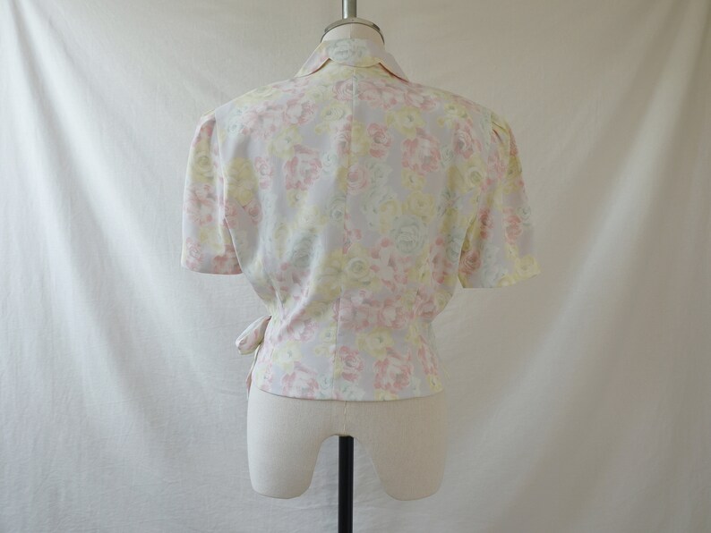 May include: A white blouse with a floral print in shades of pink, yellow, and green. The blouse has a wrap style and short sleeves.