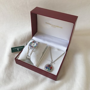 May include: A red box with a white interior containing a silver watch with a colorful face and a silver necklace with a colorful pendant. The box has the text "Gianfranco Toscani Italy" printed on the lid.