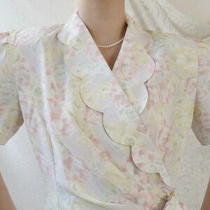 May include: A white, pink, and yellow floral print wrap blouse with a scalloped collar.
