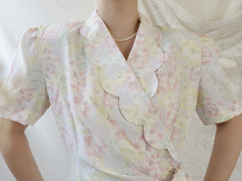 May include: A white, pink, and yellow floral print wrap blouse with a scalloped collar.