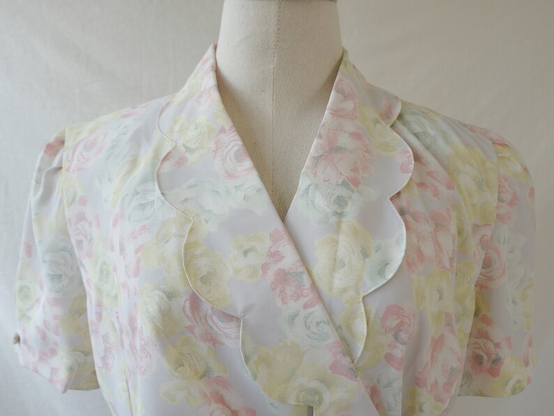 May include: A white blouse with a scalloped collar and a floral print in shades of pink, yellow, and green.