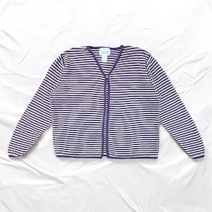 Könnte beinhalten: Ein horizontal gestreifter Cardigan in Weiß und Lila. Der Pullover hat einen V-Ausschnitt, lange Ärmel und einen Knopfverschluss. Die Einfassung und der Knopfverschluss sind lila. Das Etikett lautet "Christopher & Banks".