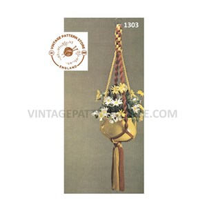 Peut inclure: Un porte-plante en macramé avec un cordon jaune et rouge. Le porte-plante est muni d'un pot jaune avec des fleurs blanches. L'image comprend le texte "1303" et le logo "Vintage Pattern Store England".