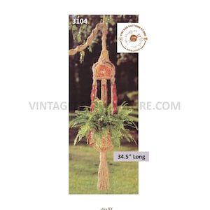 May include: A macrame plant hanger, approximately 87.6 cm long, with a fern plant inside. The hanger is made of natural-colored rope and features a decorative design with red accents. The image includes the text "Vintage Pattern Store England".