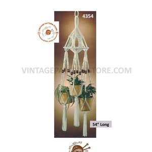 May include: White macrame plant hanger with three hanging pots and wooden beads. The hanger is 54 inches long. Vintage Pattern Store logo is at the bottom of the image.