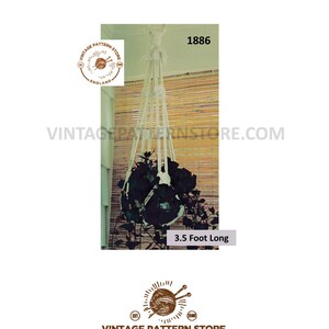 Op de afbeelding: Een witte macramé plantenhanger met een lengte van 1,07 meter. De hanger houdt een potplant met groene bladeren vast. De afbeelding bevat de tekst "Vintage Pattern Store England" en "1886".