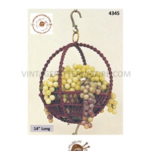 May include: A 14-inch long macrame hanging basket with a grape design. The basket is made of maroon cord and is hanging from a metal hook. The basket is filled with faux grapes in shades of purple and green.