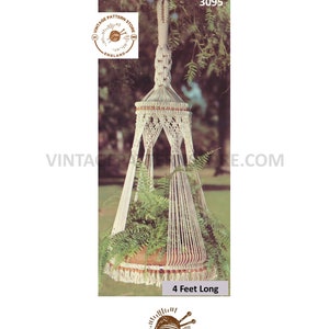 Op de afbeelding: Een witte macramé plantenhanger met een ontwerp van 1,2 meter lang. De hanger heeft de vorm van een bel met een puntige bovenkant. De hanger hangt aan een tak. De afbeelding bevat de tekst "VINTAGE PATTERN STORE ENGLAND" en "3095".