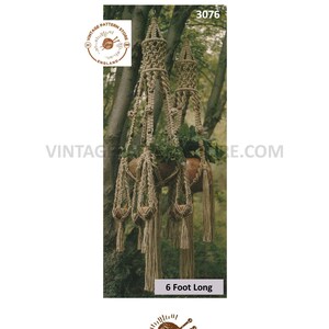May include: A macrame plant hanger with two tiers, made of natural fibre rope, with a 6 foot length. The hanger is shown hanging from a tree branch in a natural setting.