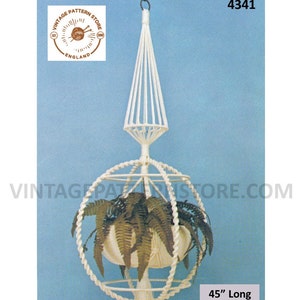 May include: White macrame hanging planter with a spherical base and a pointed top. The planter is 45 inches long and is shown with a green plant inside.