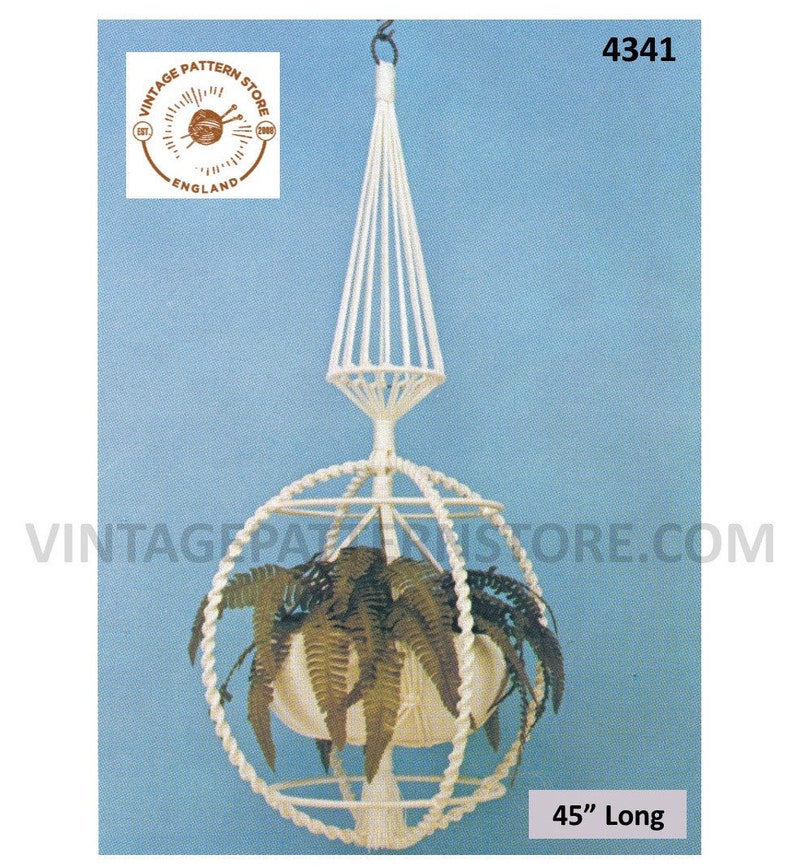 May include: White macrame hanging planter with a spherical base and a pointed top. The planter is 45 inches long and is shown with a green plant inside.