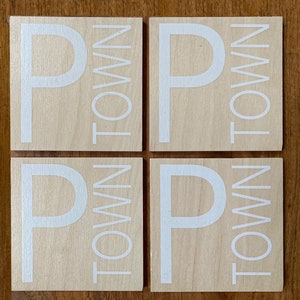 May include: Four wooden coasters with the word "P TOWN" printed in white on each coaster.