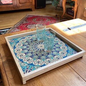 May include: A wooden serving tray with a blue and white geometric pattern. Two clear glass cups are on the tray.