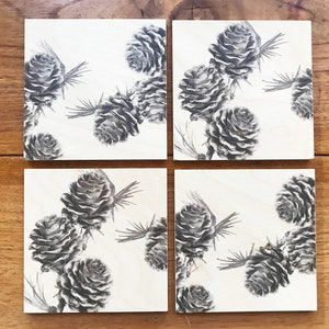 Puede incluir: Juego de cuatro posavasos cuadrados con una ilustración en blanco y negro de piñas sobre un fondo blanco.