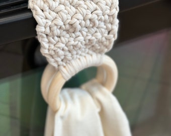 Puede incluir: Un anillo de toalla de crochet blanco con un anillo de madera. El anillo de toalla está colgado en una superficie de metal negro.