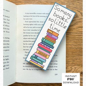 May include: A colorful, cross-stitched bookmark with the text "So many books, so little time" and a stack of books in various colors. The bookmark is lying on an open book.