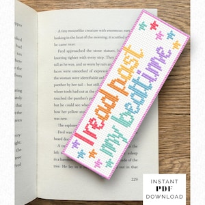 以下が含まれることがあります： カラフルなクロスステッチで「I read past my bedtime」と書かれた手作りのブックマーク。 ピンクの縁と星のアクセントが付いたブックマークが、開いた本の上に置かれています。