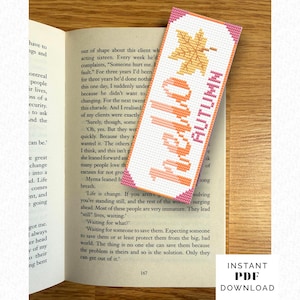 May include: A rectangular cross-stitch bookmark featuring a white background with a pink chevron border. The design includes a yellow maple leaf and the orange text "hello" stacked vertically next to the pink text "AUTUMN" in a block font.