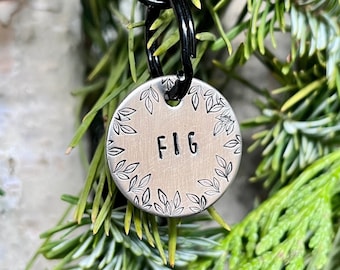May include: Silver round pet tag with a leafy border and the name "FIG" engraved in the center.