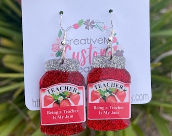 Könnte beinhalten: Paar Ohrhänger in Form von Marmeladengläsern. Die roten Ohrringe haben silberne Glitzerdeckel und Etiketten mit dem Wort "TEACHER" und dem Satz "Being a Teacher Is My Jam".