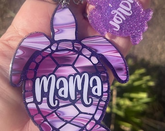 May include: Purple and white marbled turtle keychain with the word "mama" on it. A smaller purple glitter turtle keychain with the word "joni" is attached to the larger turtle keychain.