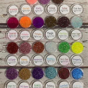 May include: A collection of 30 small jars filled with various colors of ultra-fine glitter. Each jar has a label with the name of the glitter color and the words "Ultrafine Glitter".